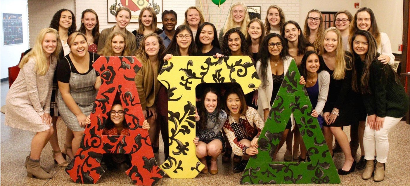 Members of Alpha Gamma Delta sorority pose in front of their letters.